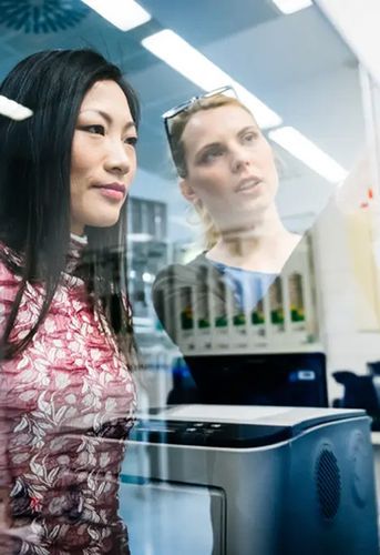 Two female engineers discussing a project in an industrial office while looking at documents pinned on a glass wall